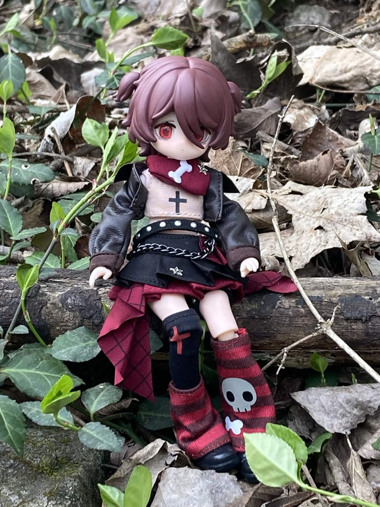 Elizabeth sitting outside on a branch thats on the ground. There are dead leaves and vines around her.