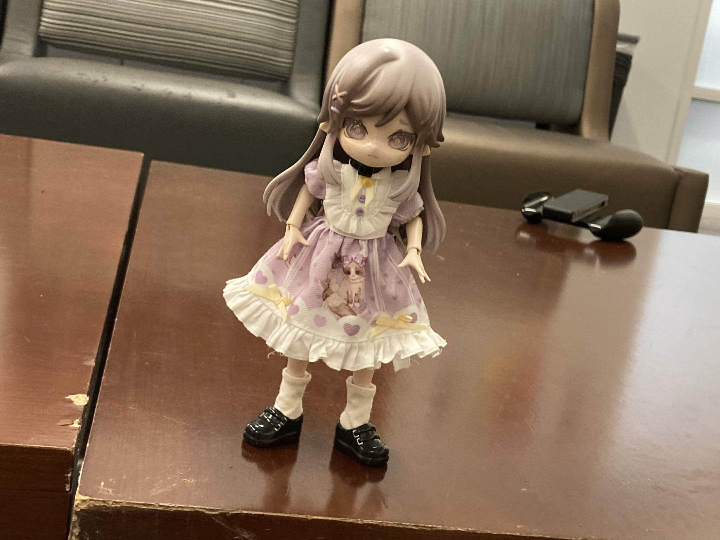 Teacup, a blind box ball-jointed doll who wears a purple kitty-themed dress, stands on a table.