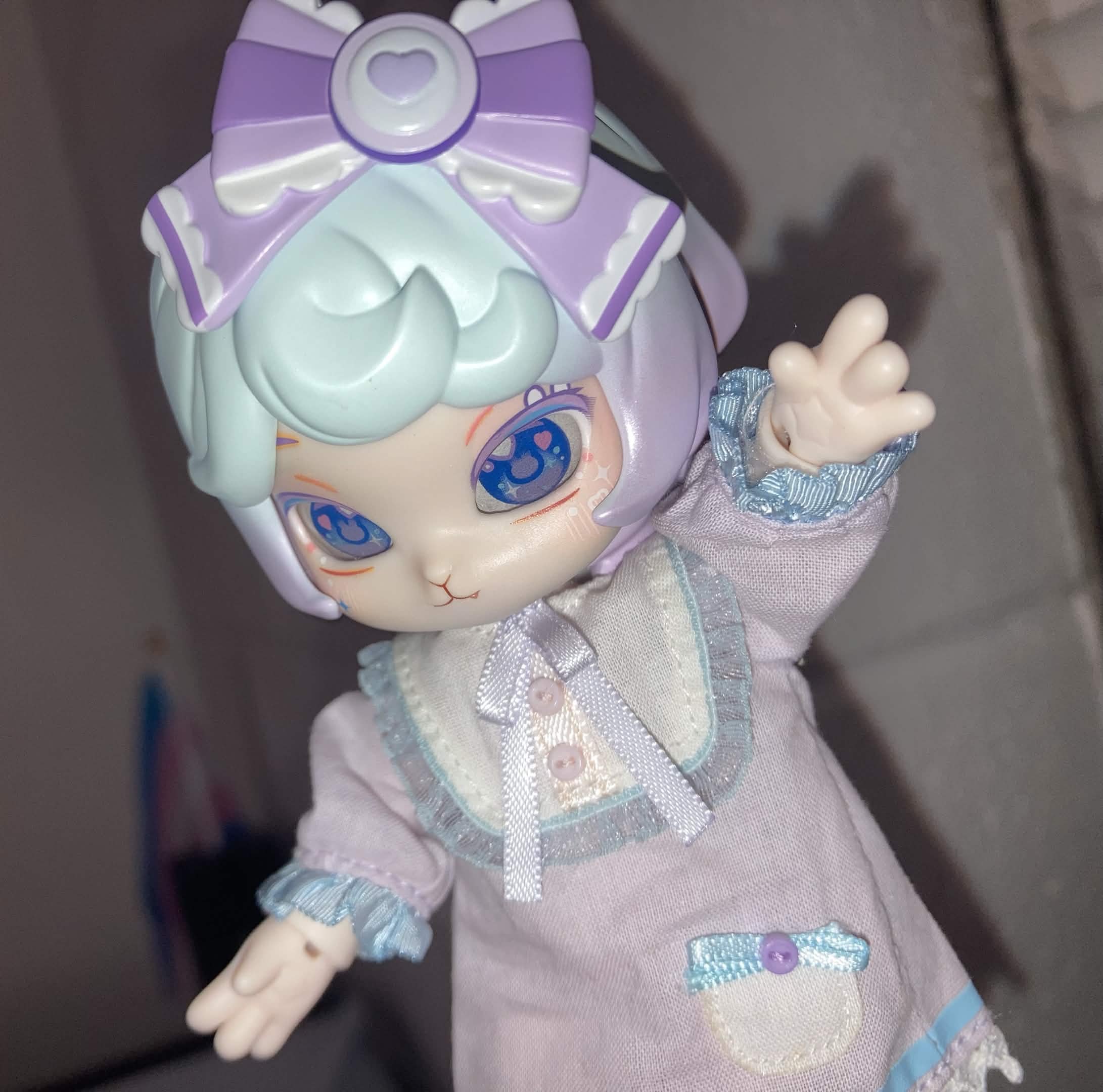 Taro, a rabbit-like doll with blue and purple hair wearing a large, purple bow and a purple nightgown poses toward the camera.