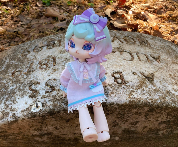 Taro wears a light-puple nightgown with blue accents. She is looking left while sitting on a small gravestone.