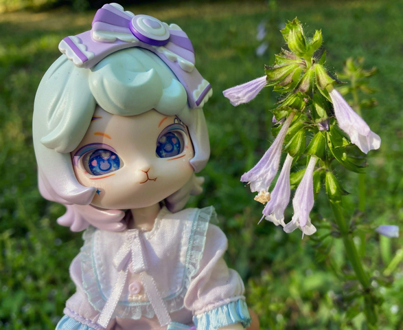Taro posing beside some light colored bell-shaped flowers. They are a similar color to her dress.